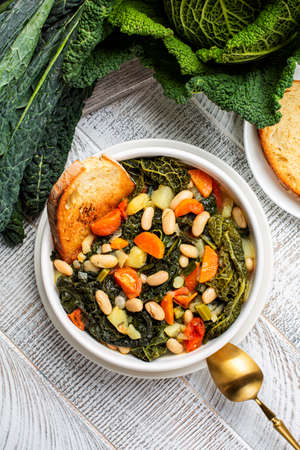 Tuscan bread soup made with toasted bread and vegetables. Ribollita. Cannellini beans, lacinato kale, cabbage verza, carrot, celery, potatoes, and onion. Itralian food. Vertical image. Directly above.の写真素材