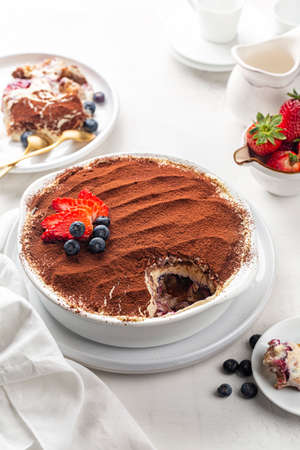 Eating Tiramisu with strawberries and blueberries and berry layer, Italian dessert with ladyfinger biscuits, coffee and marscapone cheese in a casserole, powdered with cacao. Homemade.の写真素材