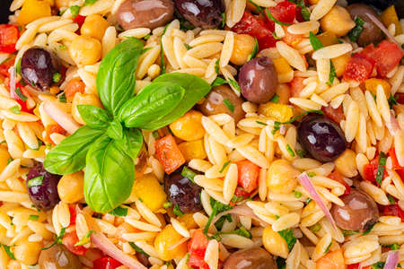 Food background. Close-up of Orzo pasta salad with vegetables, olive taggiasche, tomato, bell pepper, chickpeas, red onion, and basil.の写真素材