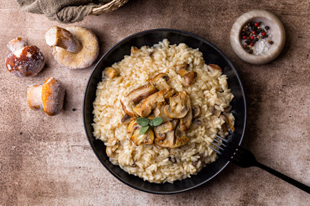 Risotto with porcini and champignon mushrooms in a black plate on brown background, directly above. Frozen raw whole mushrooms.の写真素材