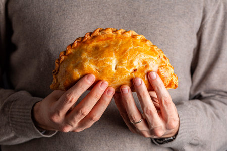 Man hands holding cornish pasty, meat turnover or pie, with filling, beef, carrot, and potato, or empanada.の写真素材