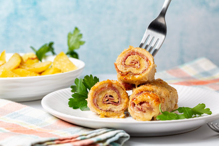 Eating chicken breast roll ups stuffed with cheese and ham, baked potato on a background. Light blue...
