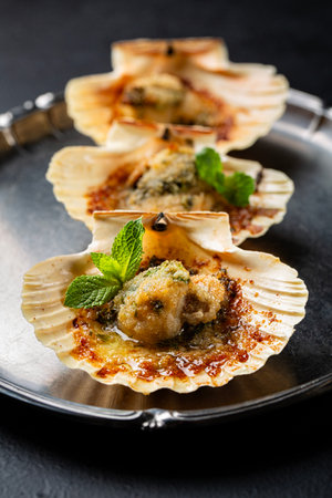 Close-up of baked scallops with breadcrumbs, lime, parsley and mint. Dark background. Vertical image.の写真素材