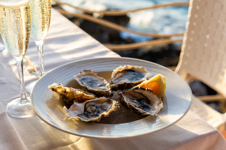 Romantic outdoor dinner with wine and seafood by the seaside. Plate with Raw Oysters with lemon and...
