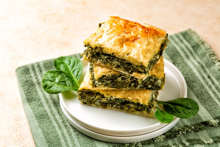 Stack of Spanakopita piece of pie, homemade Greek savory spinach pastry. It contains feta cheese, chopped spinach, green, egg, layered in phyllo or filo dought. Light beige background with green napkin.の写真素材
