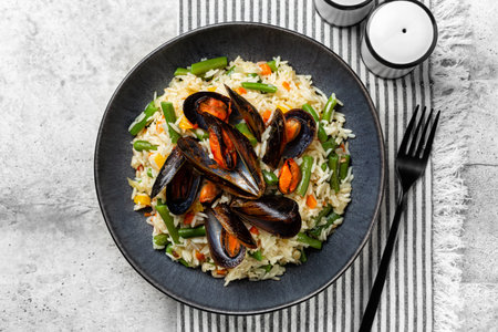 Top view of dark grey plate with hot mussels made with tomato and wine,  with fried long rice and vegetables, green beans, carrot, bell pepper.の写真素材