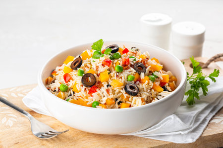Rice with fresh vegetables, bell bebber, tomato, green pea, black olives and olive oil,  on a white table. Table setting, white background, copy space.の写真素材