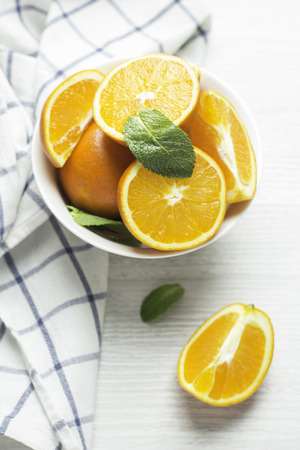 oranges in a white cup and mint leaves on a white wooden background top viewの写真素材