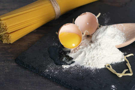 broken egg, flour and spaghetti on a black background