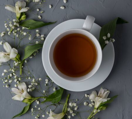 white cup of tea on plate with flowers on gray table top viewの写真素材