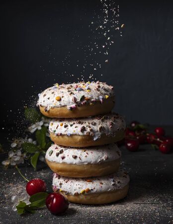 some delicious donuts at each other with cherry berry on dark background colorful sprinkles front artの写真素材