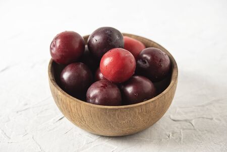 sweet fresh delicious red plums on bowl white wood table summer fruitsの写真素材
