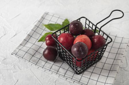 weet fresh delicious red plums on black basket white wood table summer fruitsの写真素材