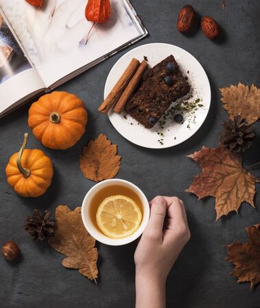 sweet chocolate brownie cup of tea hand with lemon pumpkins, yellow foliage and book hygge  mood flat lay autumn top viewの写真素材
