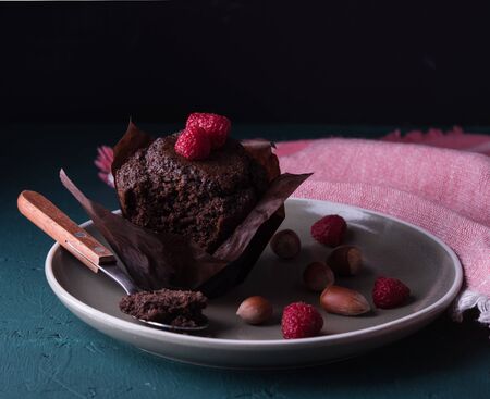 sweet chocolate muffin with raspberry and spoon on plate dark background close upの写真素材