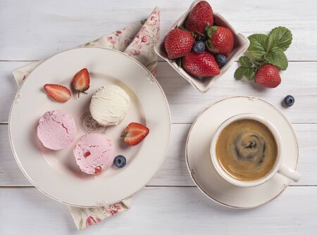 some sweet balls  ice cream vanilla and strawberry  with fresh berries on plate  with cup of coffee village wood background top viewの写真素材