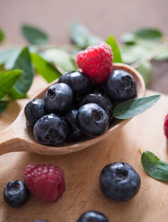 fresh sweet blueberry and raspberry on the wooden spoon rustic village summer berry macro close upの写真素材