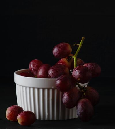 fresh sweet  yet red grape on the white bowl on wood table dark background dark moodの写真素材