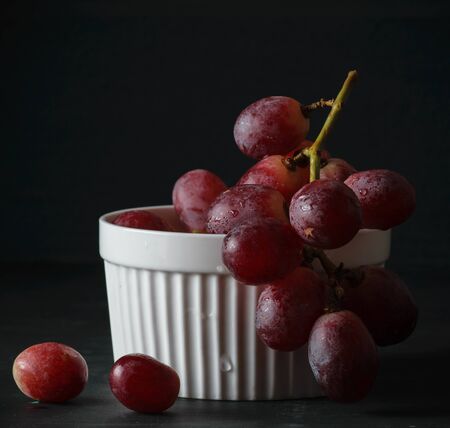 fresh sweet  yet red grape on the white bowl on wood table dark background dark moodの写真素材