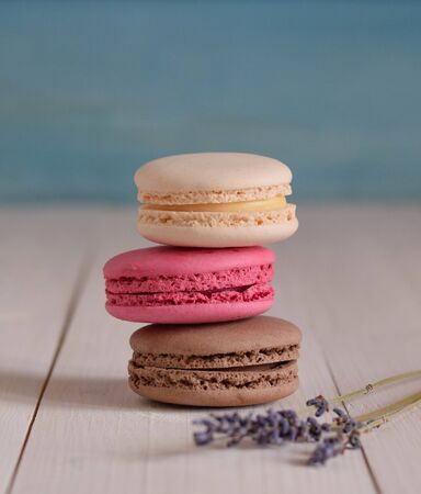 three colored sweet macaroons on the wood light table with twig lavender close up pastel frontの写真素材