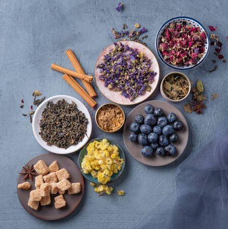 some plate with aromatic herbal tea chamomile, lavender and rose, sugar and blueberries loose on blue table top viewの写真素材