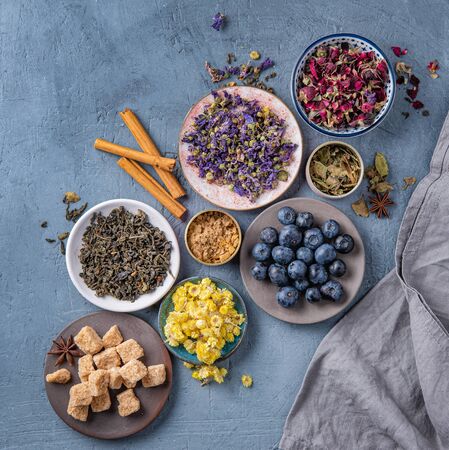 some plate with aromatic herbal tea chamomile, lavender and rose, sugar and blueberries loose on blue table top viewの写真素材