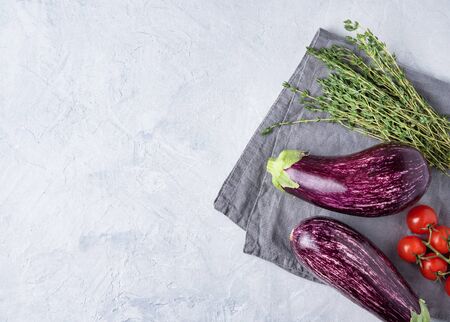 two juicy eggplants  graffiti  with cherry tomatoes thyme  lie on a gray napkin on a blue concrete table top view copy spaceの写真素材