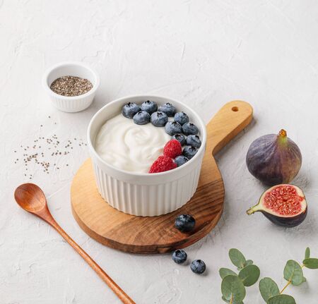 natural healthy superfood fermented yogurt with blueberry, figs, chia seeds and raspberry in white  bowl on light gray table. Image is copy space and top viewの写真素材