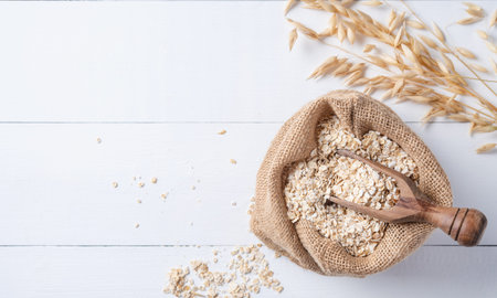 Healthy and organic oat flakes in sack with wood spoon and branch on the white wooden table. Vegan...