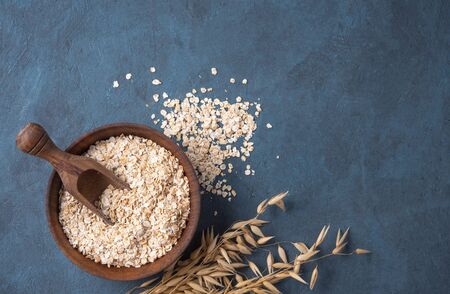 Healthy and organic oat flakes in wood bowl with spoon and branch on the dark blue wooden table. Vegan food. Image is copy space, vertical orientation and top viewの写真素材