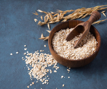 Healthy and organic oat flakes in wood bowl with spoon and branch on the dark blue wooden table....
