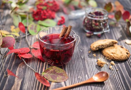 Red hot  cup of tea and autumn colorful leaves lie on the wooden table with cinnamon stick, jam and homemade cookies.Image is close up and front viewの写真素材
