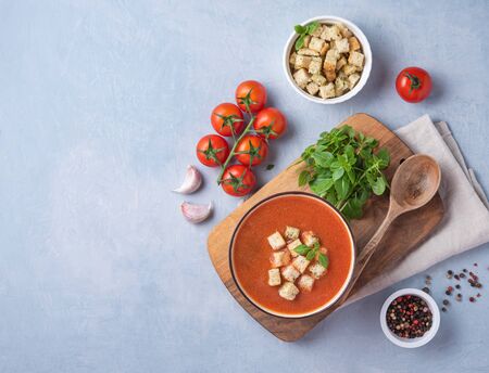 Fresh orange vegan diet tomato creme soup with crumbs, garlic, spicy and fresh  basil on wooden cutting board and blue background. Image top view and copy spaceの写真素材