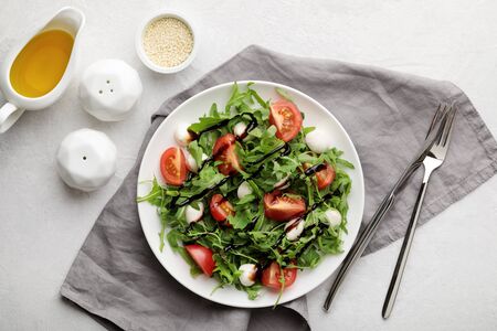 Fresh italian salad caprese with tomato mozzarella and rocket on white plate, gray napkin and white background. Top viewの写真素材