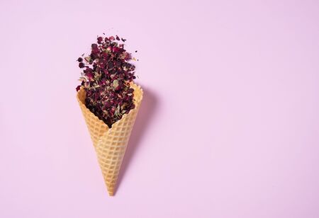 dry rose tea falls out of a waffle cone on a pink background. Top view and copy spaceの写真素材