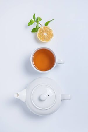 Fresh aroma cup of black tea and tea pot with lemon, mint and golden spoon on white  background. Top view and copy space. Vertical orientation.の写真素材
