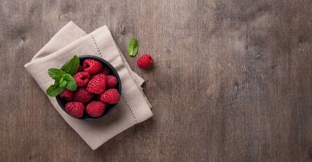 Fresh and sweet raspberry with mint in  black bowl on old vintage brown wood background. Top view and copy space.  の写真素材