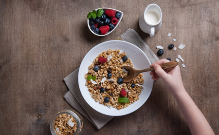 sweet granola with raspberry,  blueberry and coconut milk into white plate on wooden old brown...