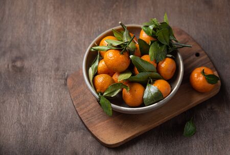 sweet juicy mini tangerines lie in a ceramic bowl on a wooden old brown table. Copy spaceの写真素材