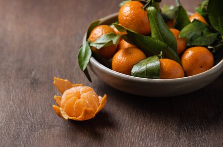 sweet juicy mini tangerines lie in a ceramic bowl on a wooden old brown table. Copy spaceの写真素材
