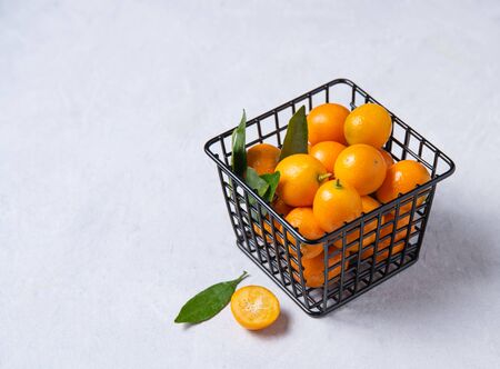juicy fresh sweet kumquats lie in a metal box on a white wooden table. Top view and copy spaceの写真素材
