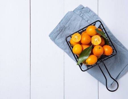 juicy fresh sweet kumquats lie in a metal box on a white wooden table. Top view and copy spaceの写真素材