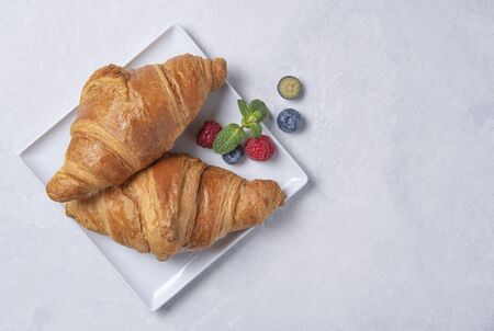 two fresh hot gluten free croissants on a white square plate with blueberries and raspberries on a grey background. Top view and copy spaceの写真素材