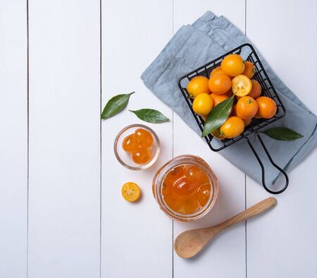 juicy fresh sweet kumquats lie in a metal box and a glass jar with jam on a white wooden table. Top view and copy spaceの写真素材