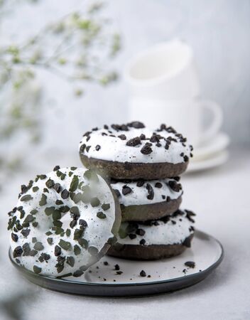 several delicious fresh hearty black and white doughnuts are stacked in a white plate on a white background with flowers of gypsophila. Spring mood. front viewの写真素材