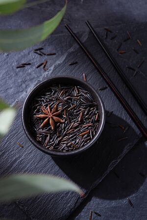 black wild  raw vegan rice in a black bowl on a slate Board with dark Chinese sticks on a black background. Dark photo and top viewの写真素材