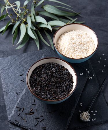 black and white raw vegan wild rice in two blue bowl on a slate Board with dark spoon on a black background.の写真素材