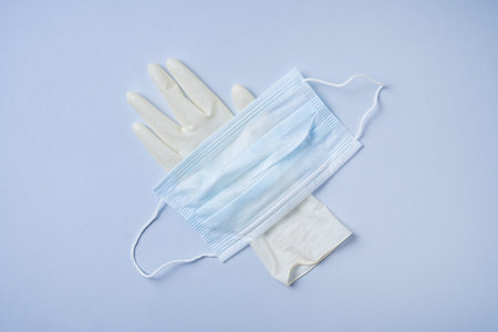 the face mask and medical glove are on a blue background. Coronavirus pandemic, essential goods,...