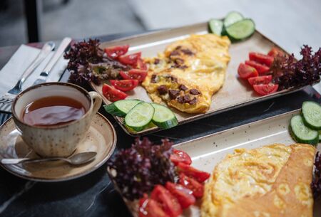 summer Breakfast in the cafe. Fried eggs with fresh vegetables and a Cup of tea on a black marble tableの写真素材