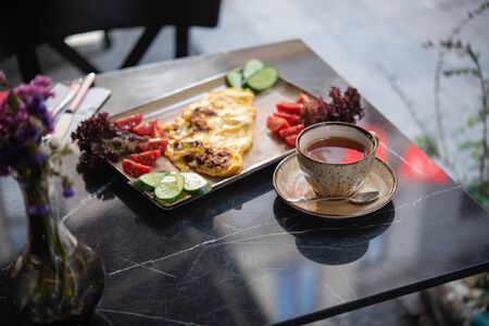 summer Breakfast in the cafe. Fried eggs with fresh vegetables and a Cup of tea on a black marble tableの写真素材